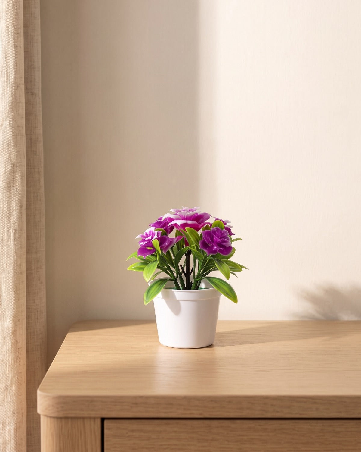 A small artificial flowering pot with purple blooms, in the white pot it comes in, on a pale oak table