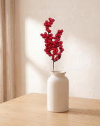 One artificial red berry branch in a plain off-white vase on a pale oak table; vase not included