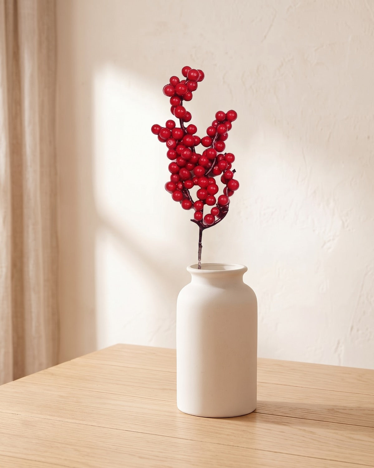 One artificial red berry branch in a plain off-white vase on a pale oak table; vase not included