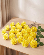 Twenty-five yellow foam rose heads on wire stems with green leaf sprays, laid out on a pale oak table