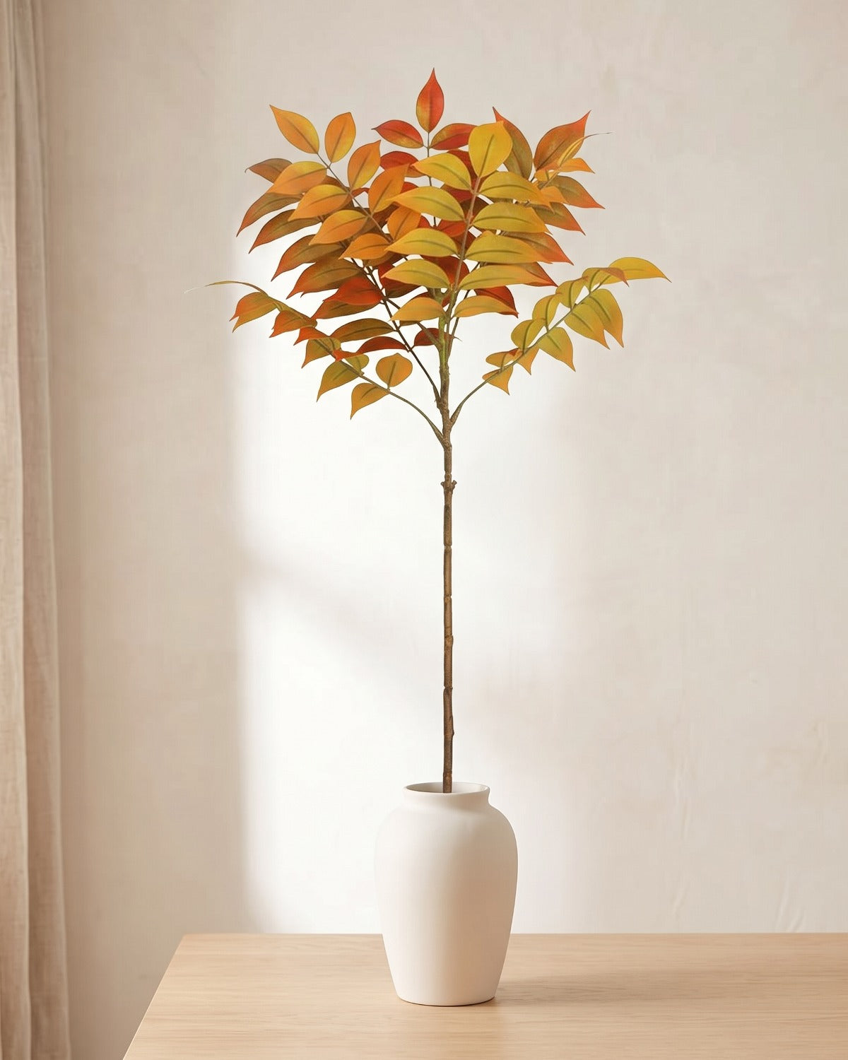 Autumn leaf artificial tree branch standing in a plain off-white vase on a pale oak table; no vase is included