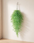 Green artificial wisteria vine hanging from a simple hook on an off-white plaster wall, its full drop clear of the floor