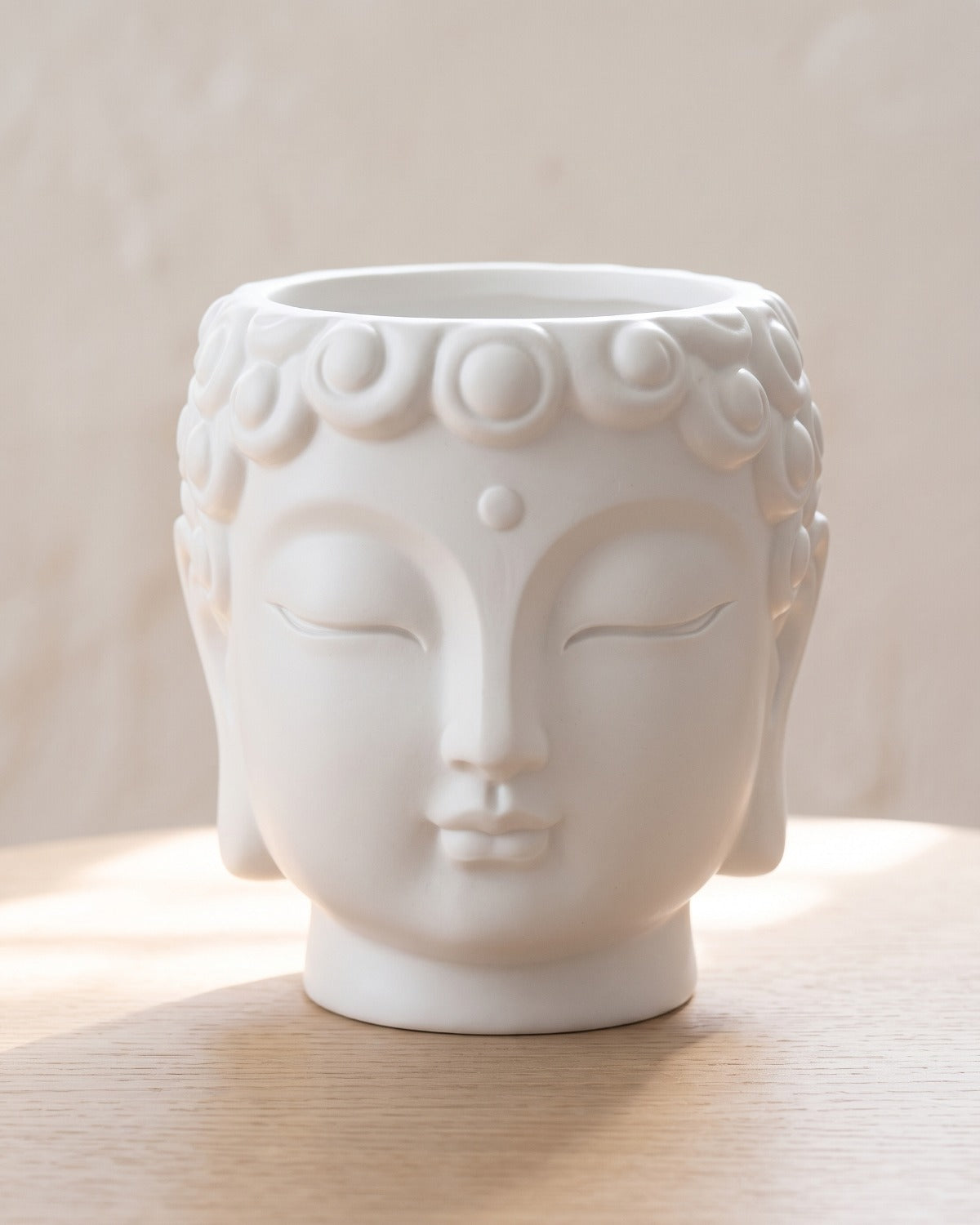 White Buddha head planter, empty on a pale oak table