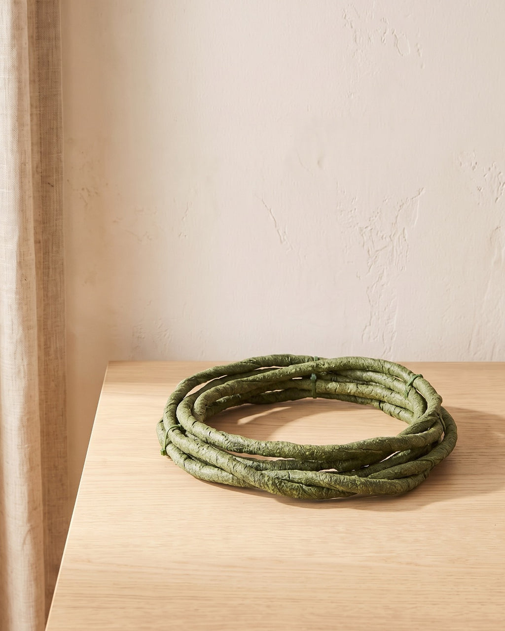 A small coil of green artificial jungle vine at its 3.3 ft length, on a pale oak table
