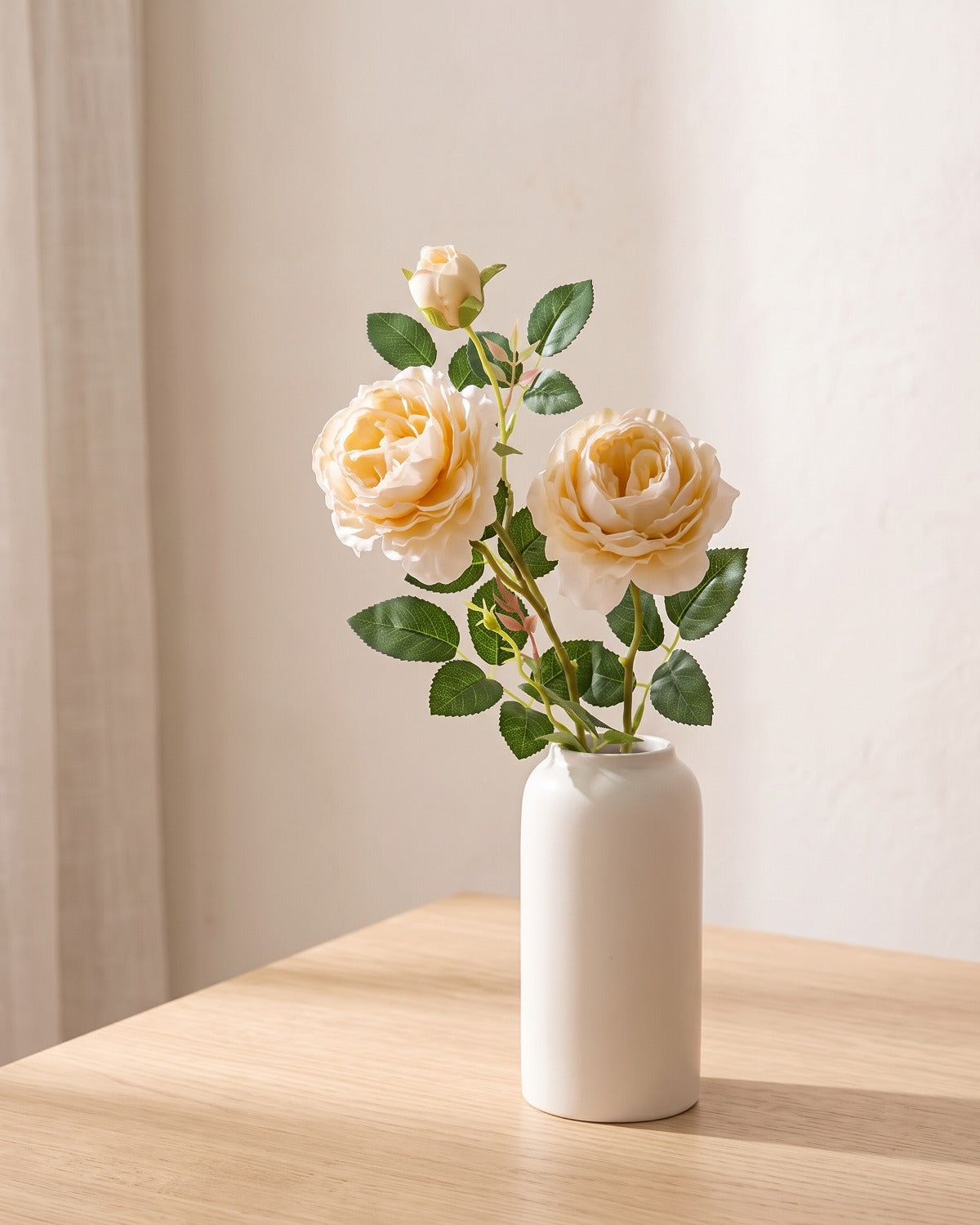 Champagne artificial rose branch standing in a plain off-white vase on a pale oak table; each order is one branch, and no vase is included