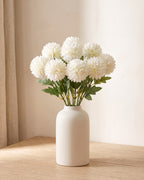 Cream White artificial pompom chrysanthemums standing in a vase on a pale oak table; no vase is included