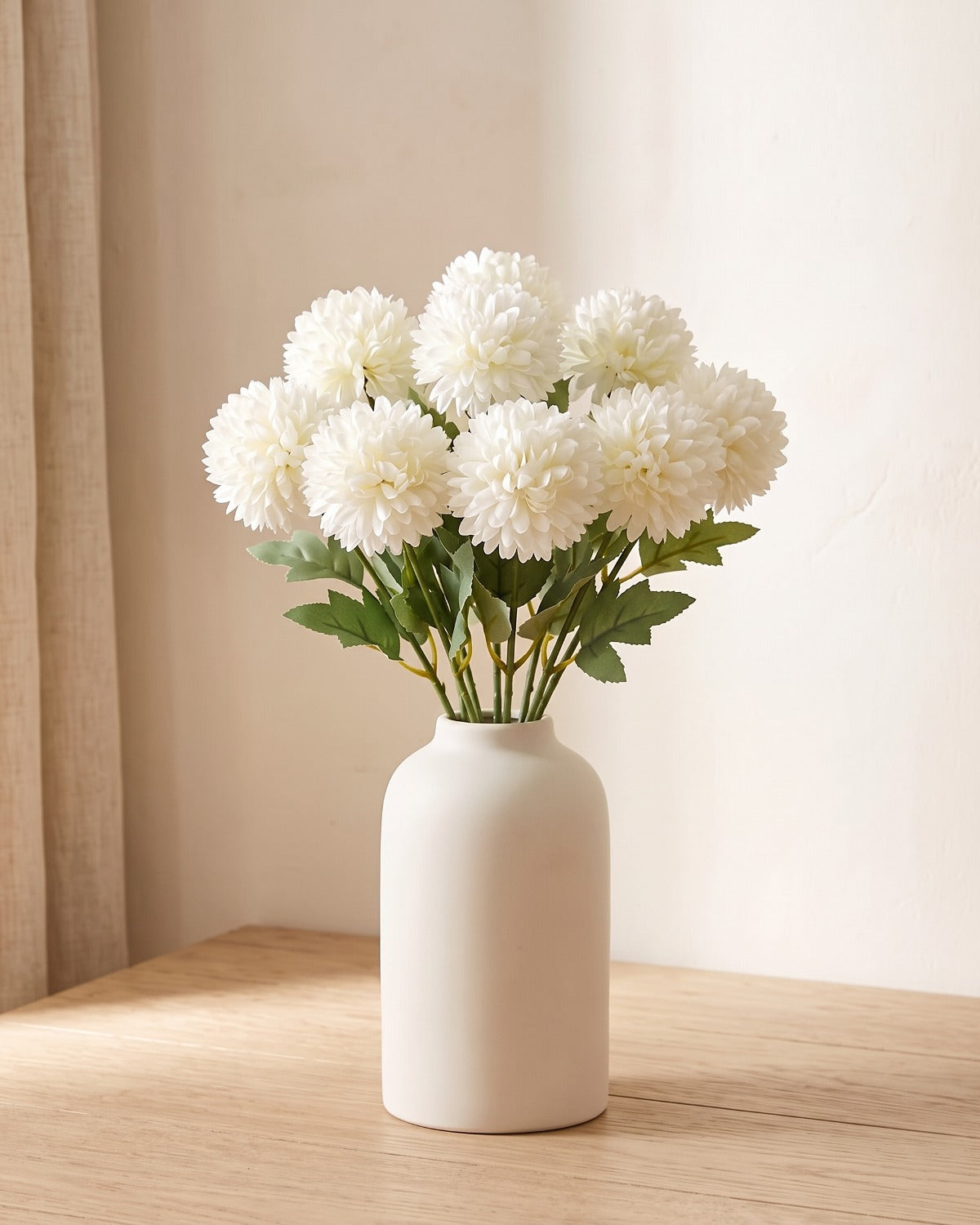 Cream White artificial pompom chrysanthemums standing in a vase on a pale oak table; no vase is included
