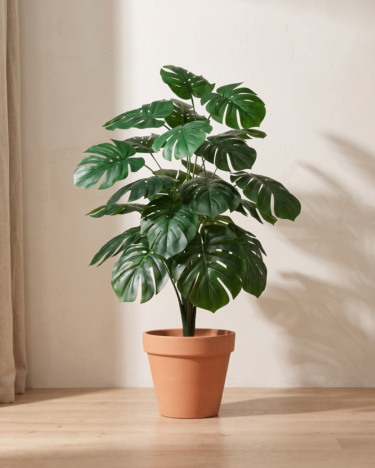 Artificial monstera bush with deeply split leaves in plain deep green, in a plain terracotta pot; pot not included