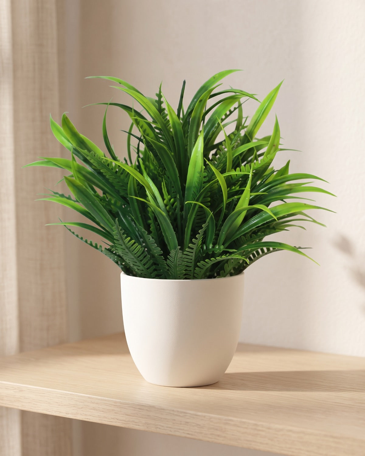 Fern style mini artificial potted plant in a plain white pot on a pale oak table