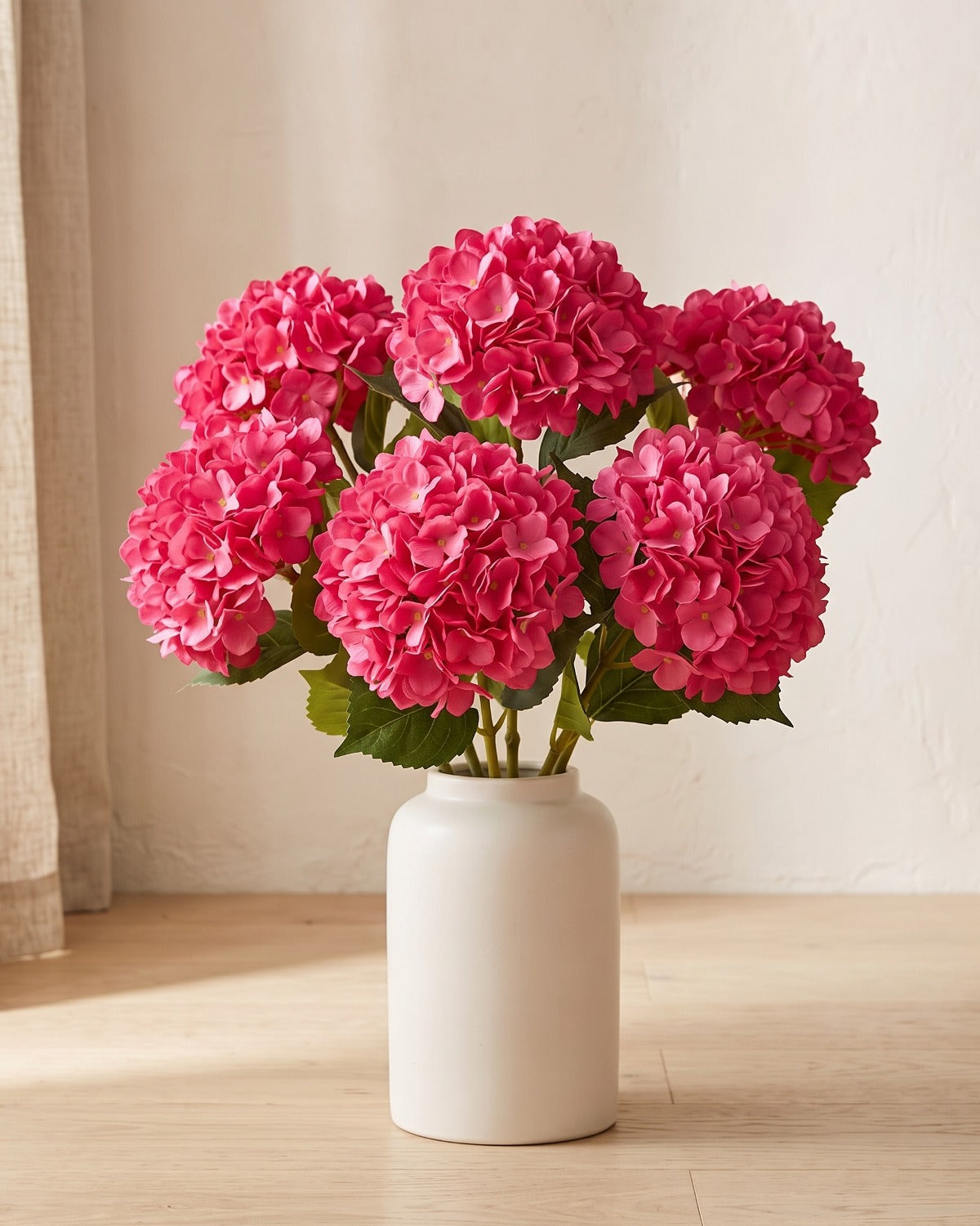 Rose Red artificial hydrangea flowers standing in a plain off-white vase on a pale oak table; no vase is included