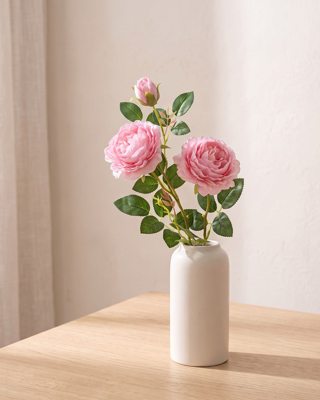 Pink artificial rose branch standing in a plain off-white vase on a pale oak table; each order is one branch, and no vase is included