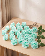 Twenty-five mint green foam rose heads on wire stems with green leaf sprays, laid out on a pale oak table