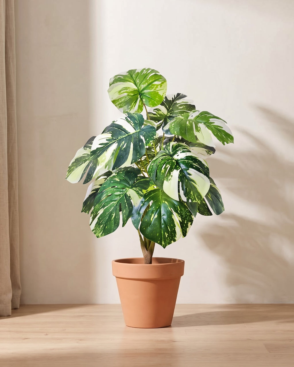 Artificial monstera bush with split leaves marbled in light and dark green, in a plain terracotta pot; pot not included