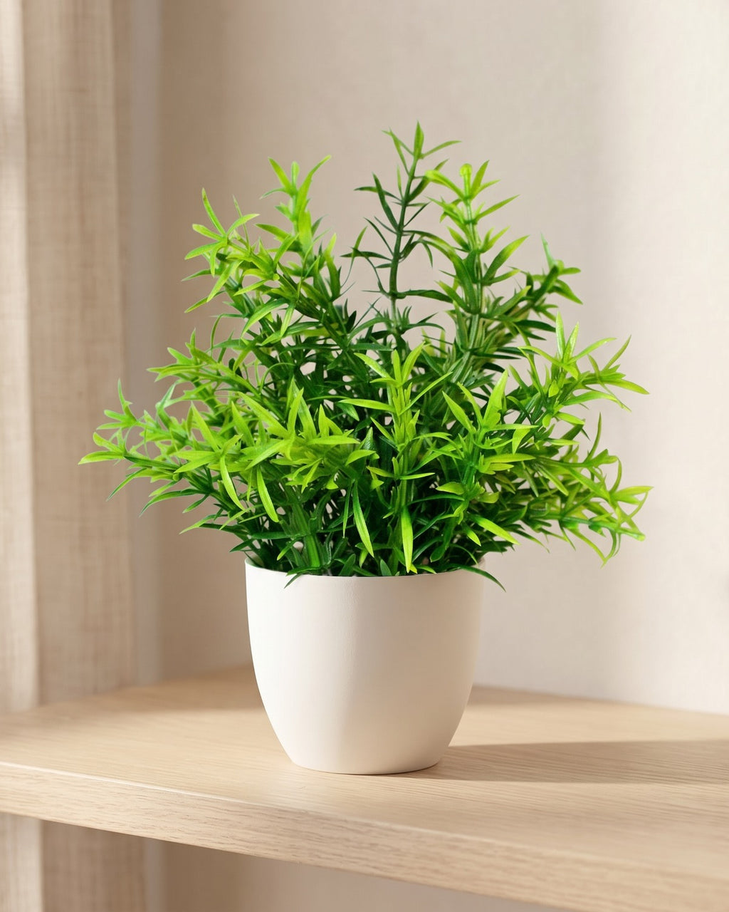 Rosemary style mini artificial potted plant in a plain white pot on a pale oak table