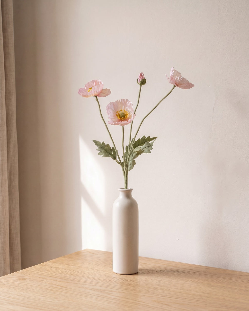 A pink opal artificial poppy stem, one stem with two open flowers and a bud, in a plain off-white bud vase on a pale oak table; vase not included
