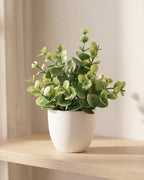Coin leaf style mini artificial potted plant in a plain white pot on a pale oak table