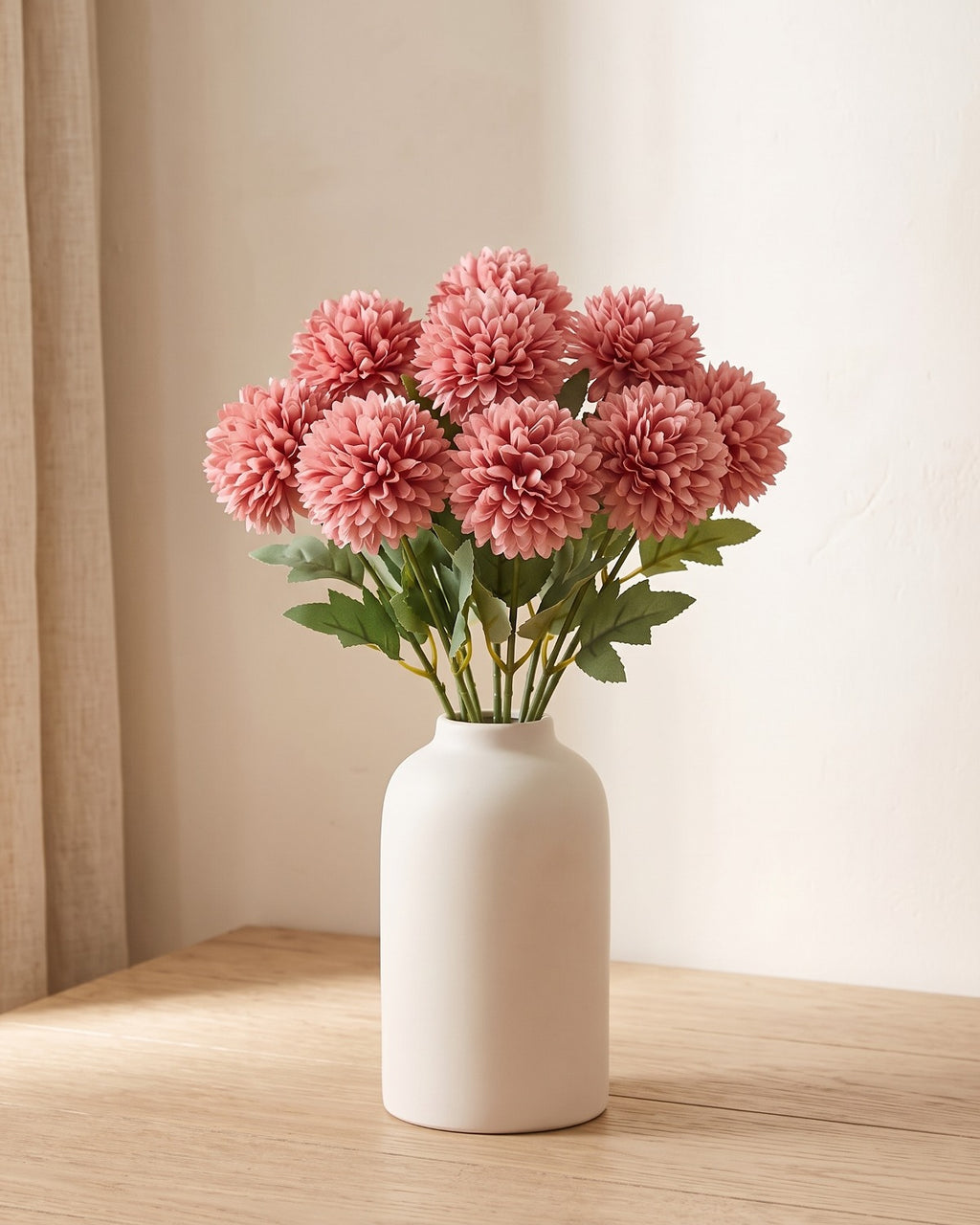 Dusty Rose artificial pompom chrysanthemums standing in a vase on a pale oak table; no vase is included