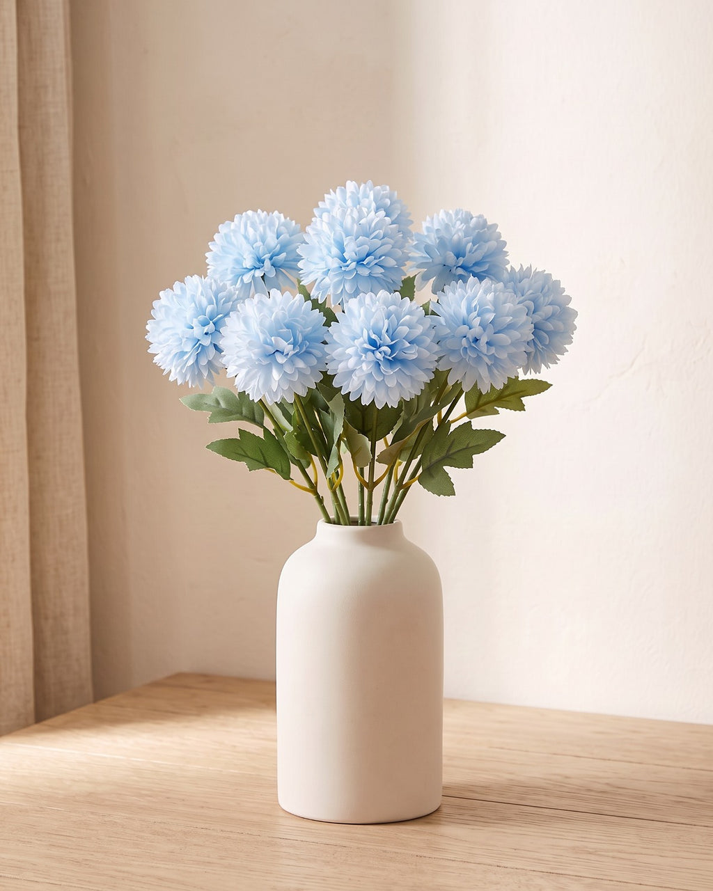 Light Blue artificial pompom chrysanthemums standing in a vase on a pale oak table; no vase is included