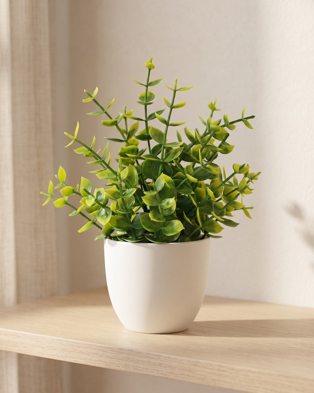 Eucalyptus style mini artificial potted plant in a plain white pot on a pale oak table