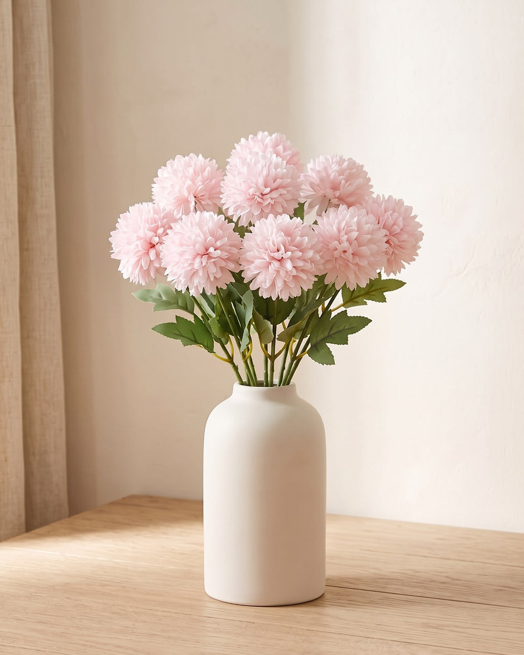 Pale Pink artificial pompom chrysanthemums standing in a vase on a pale oak table; no vase is included