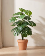 Artificial monstera bush with deeply split leaves in an even mid green, in a plain terracotta pot; pot not included