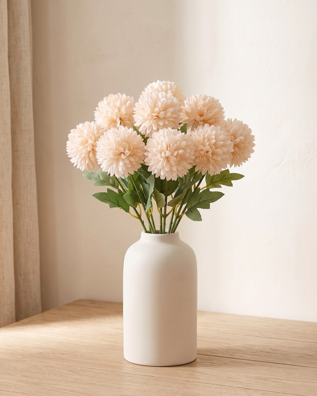 Champagne artificial pompom chrysanthemums standing in a vase on a pale oak table; no vase is included