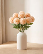 Peach artificial pompom chrysanthemums standing in a vase on a pale oak table; no vase is included
