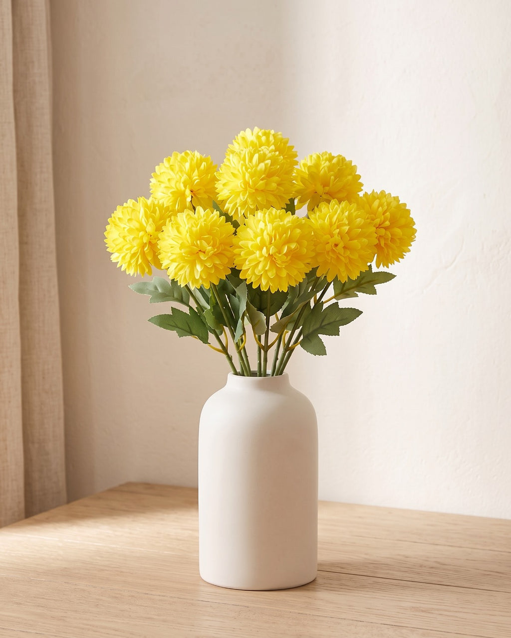 Lemon Yellow artificial pompom chrysanthemums standing in a vase on a pale oak table; no vase is included
