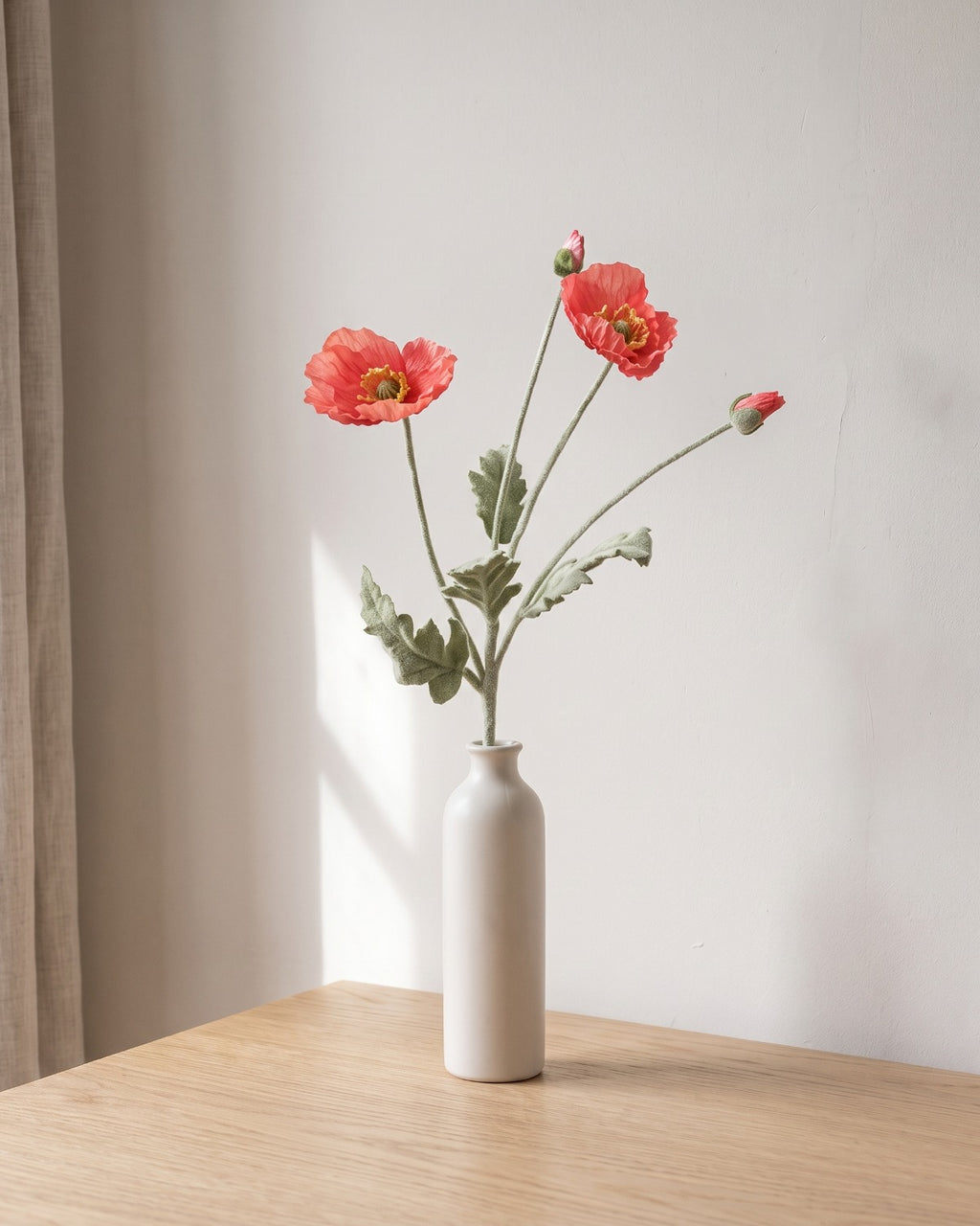 A dark coral artificial poppy stem, one stem with two open flowers and a bud, in a plain off-white bud vase on a pale oak table; vase not included
