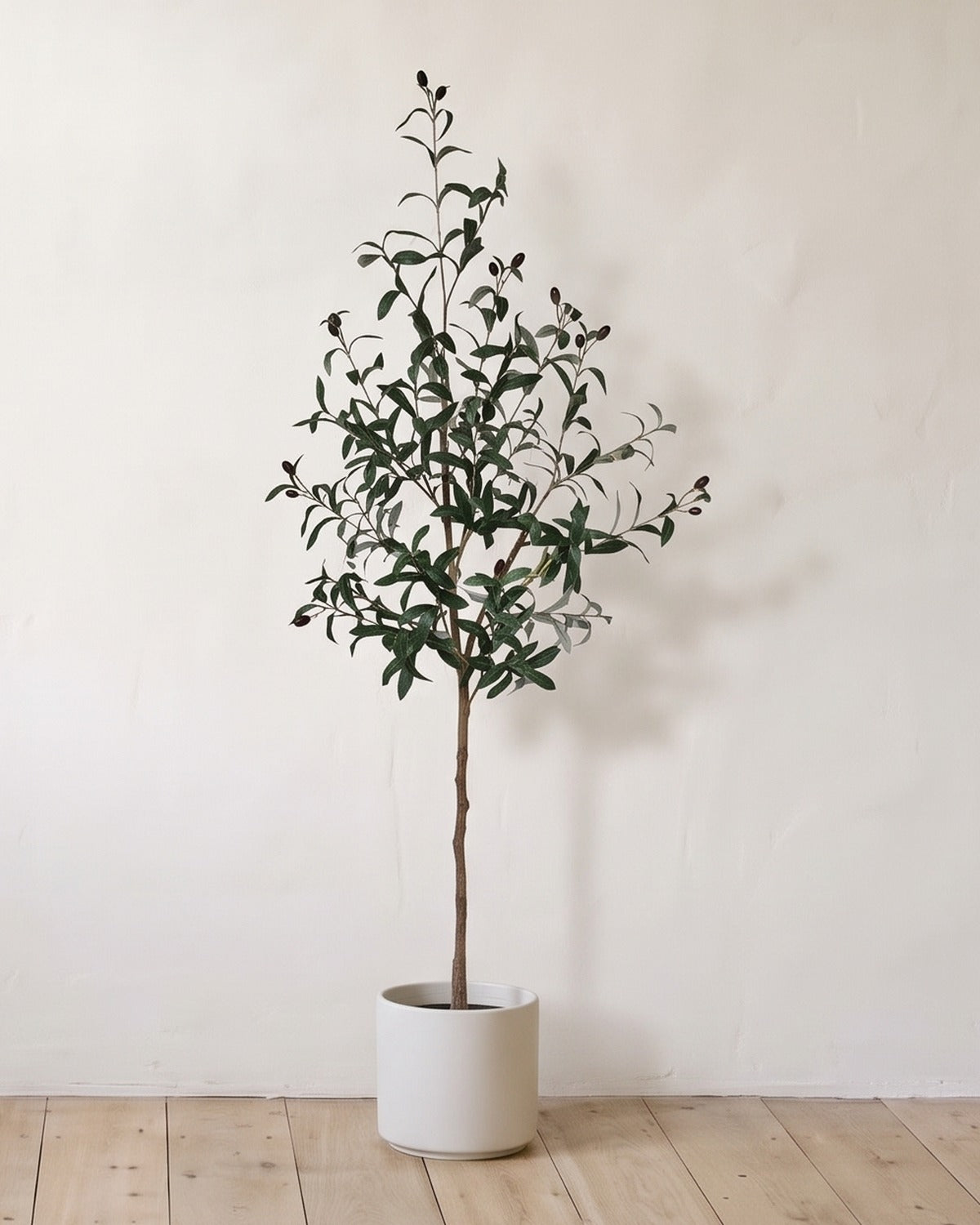 The 59 in artificial olive tree in a plain white pot, against a warm white wall; planter not included