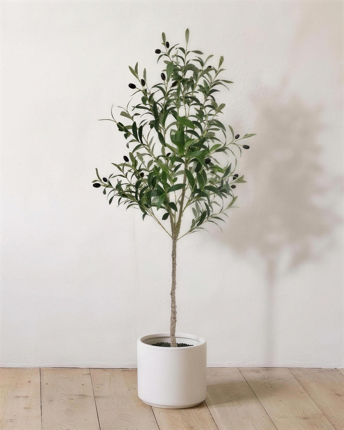 The 47 in artificial olive tree in a plain white pot, against a warm white wall; planter not included