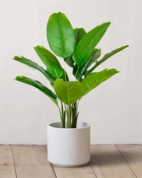The 26 in artificial bird of paradise with twelve leaves, in a plain white pot against a warm white wall; pot not included