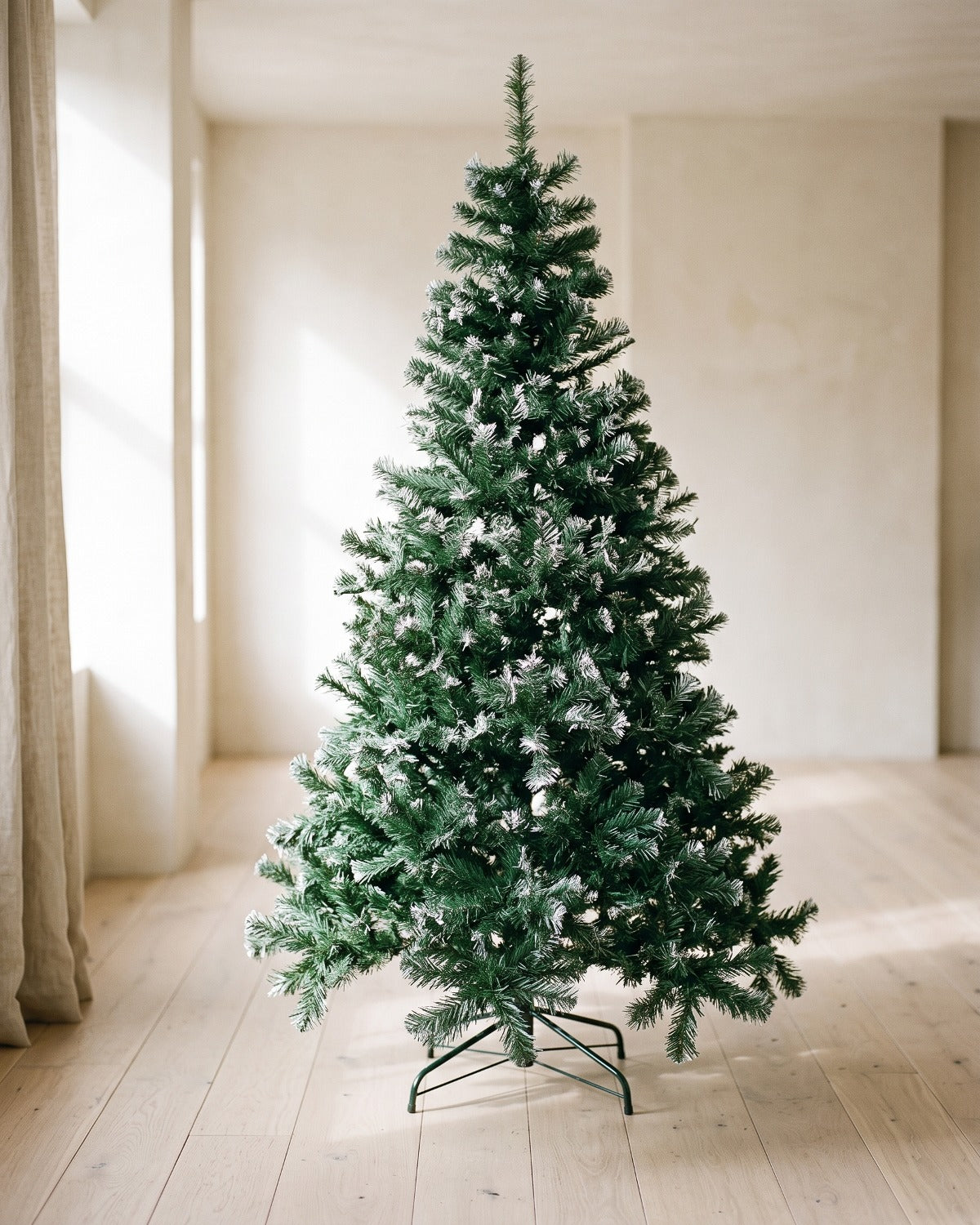 Green artificial Christmas tree with frosted white tips, undecorated, on its stand