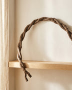 Artificial jungle vine bent into an arc across a plaster wall above an oak shelf