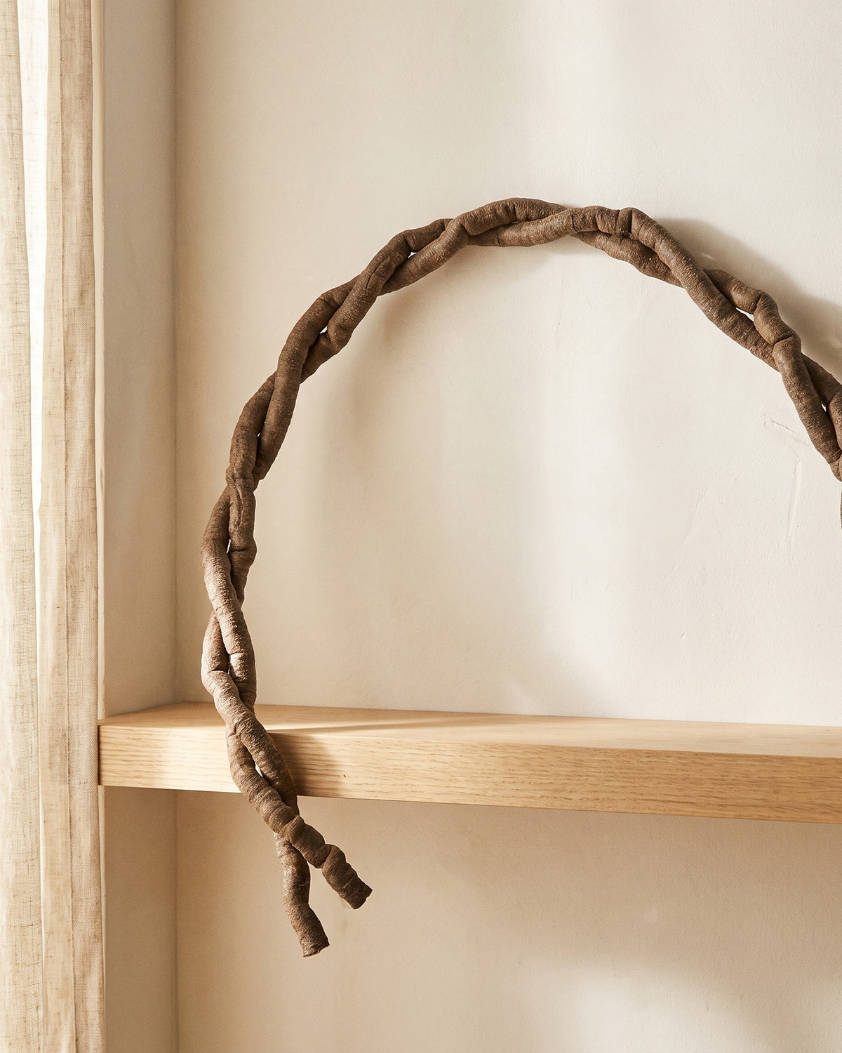 Artificial jungle vine bent into an arc across a plaster wall above an oak shelf
