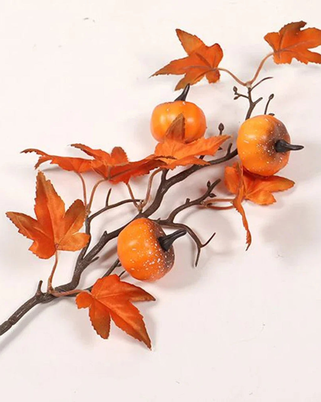 Artificial pumpkin branch with small orange pumpkins and maple leaves on marble