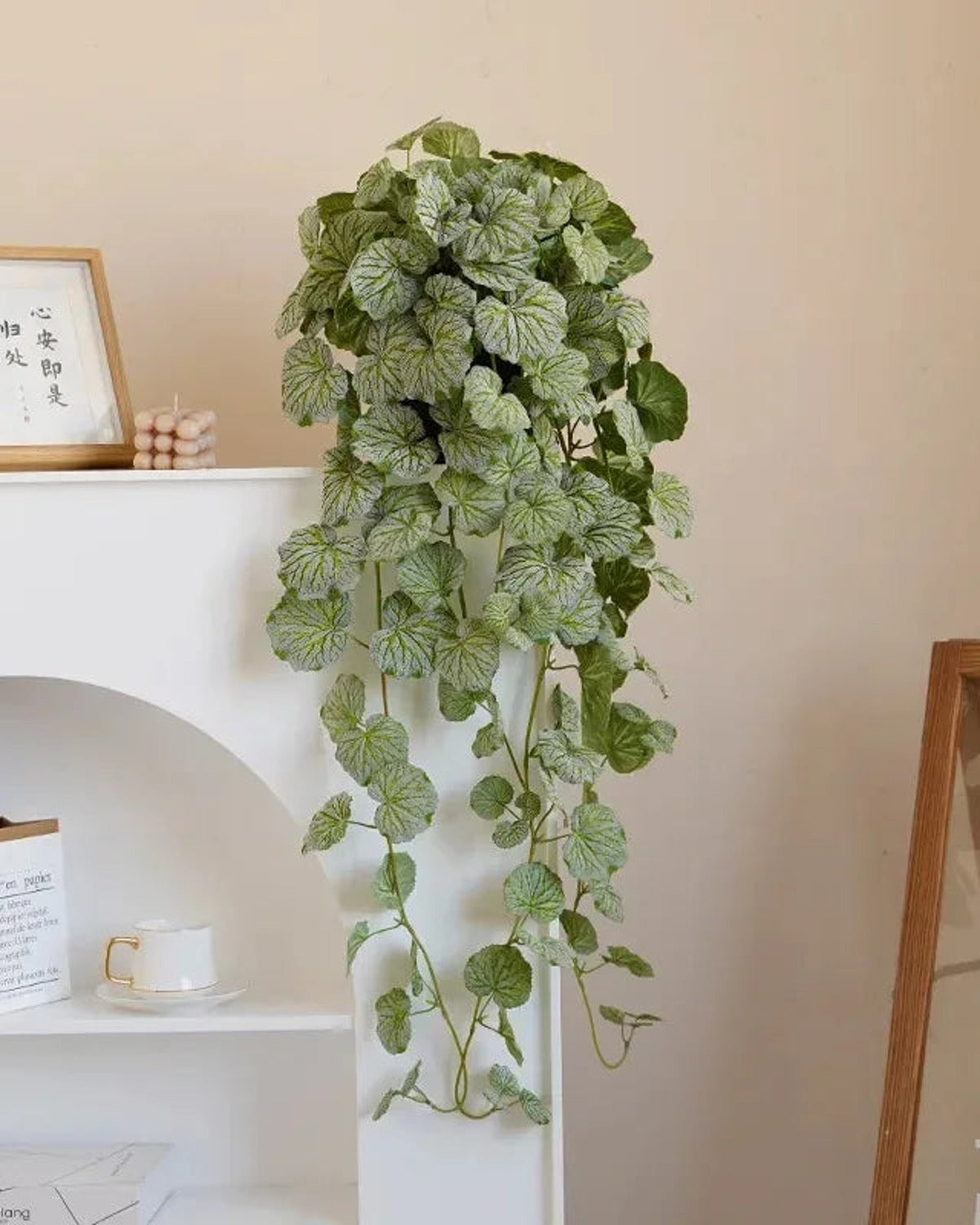 Artificial hanging begonia vine trailing from a white shelf against a peach wall