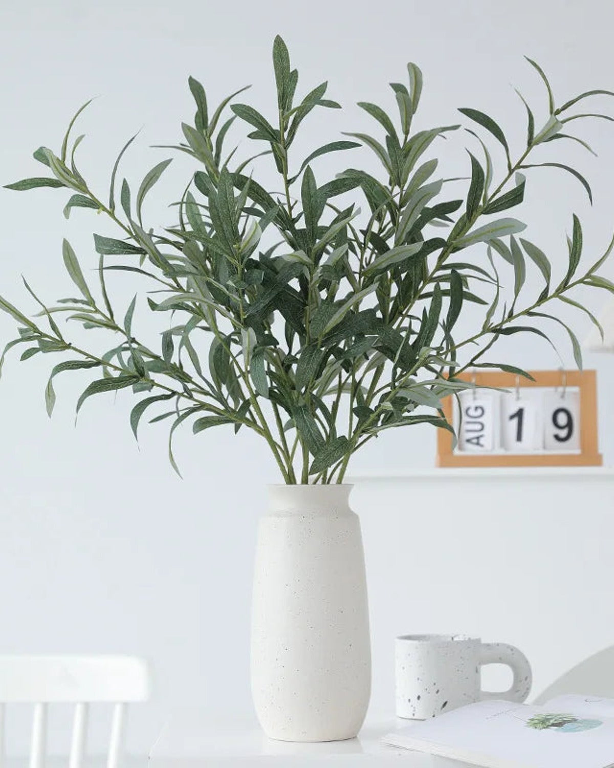 Artificial olive branches in a white vase on a desk with a calendar