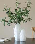 Artificial olive branches in a white leaf-shaped vase on a dark table