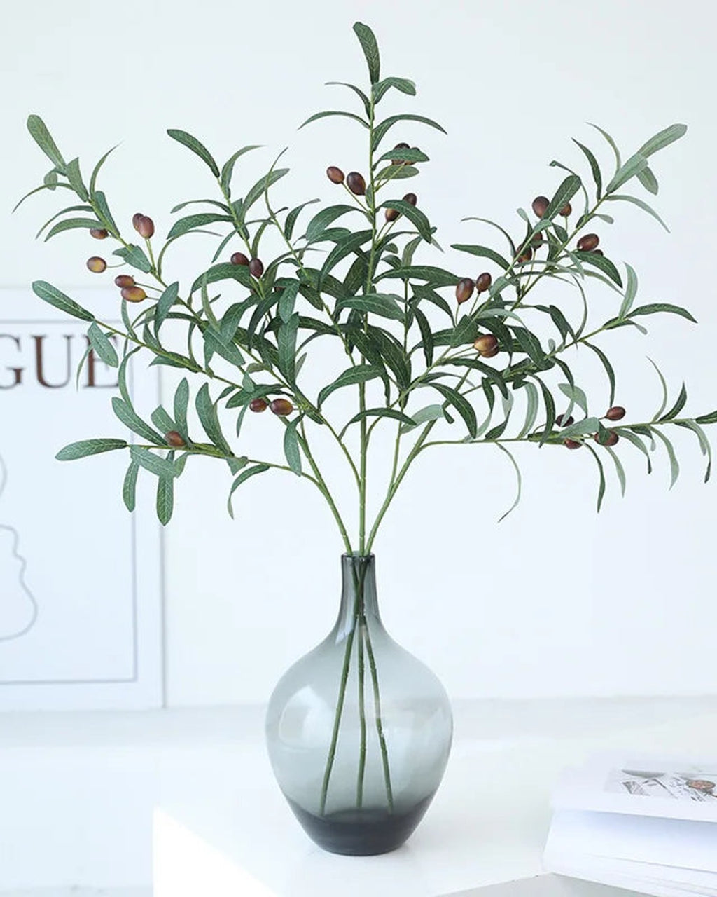 Artificial olive branches in a dark glass bottle vase