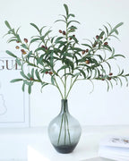Artificial olive branches in a dark glass bottle vase
