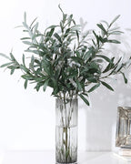 Artificial olive branches in a ribbed glass vase on a white table