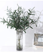 Artificial olive branches in a ribbed glass vase beside a picture frame