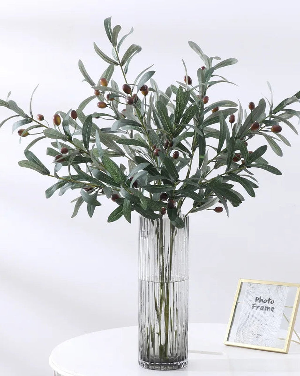 Artificial olive branches in a glass vase with the dark olives showing