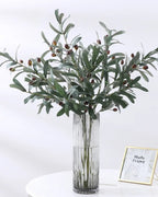 Artificial olive branches in a glass vase with the dark olives showing