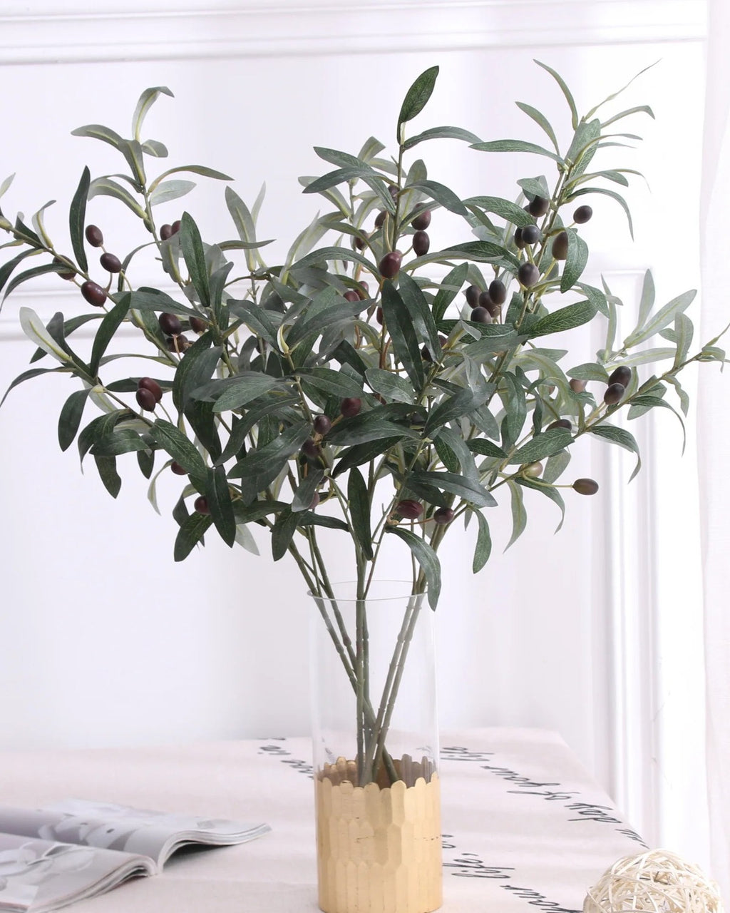 Artificial olive branches in a wooden pot on a white table