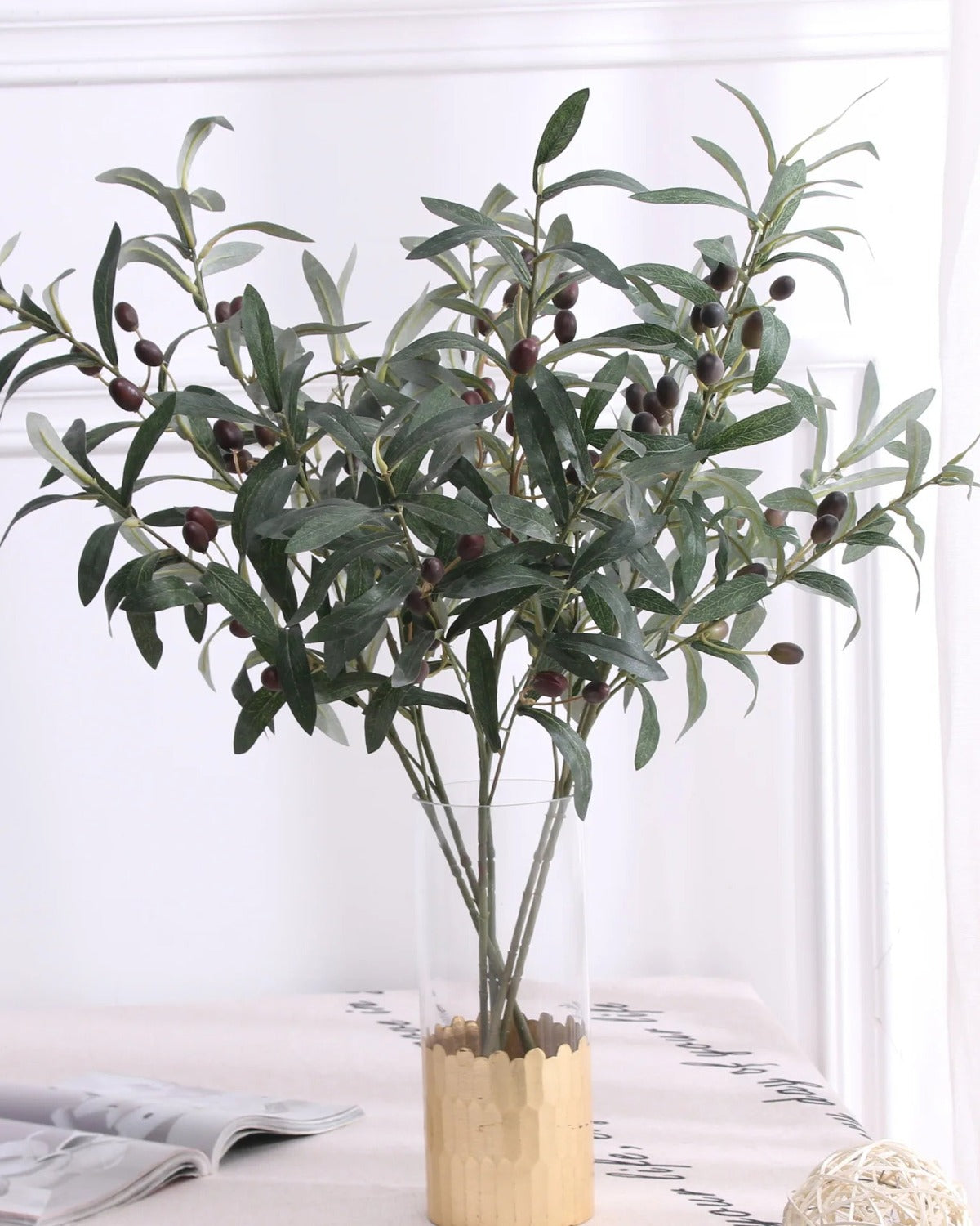 Artificial olive branches in a wooden pot on a white table