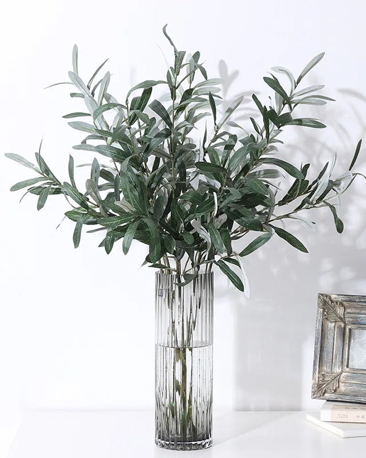Artificial olive branches in a ribbed glass vase, side view