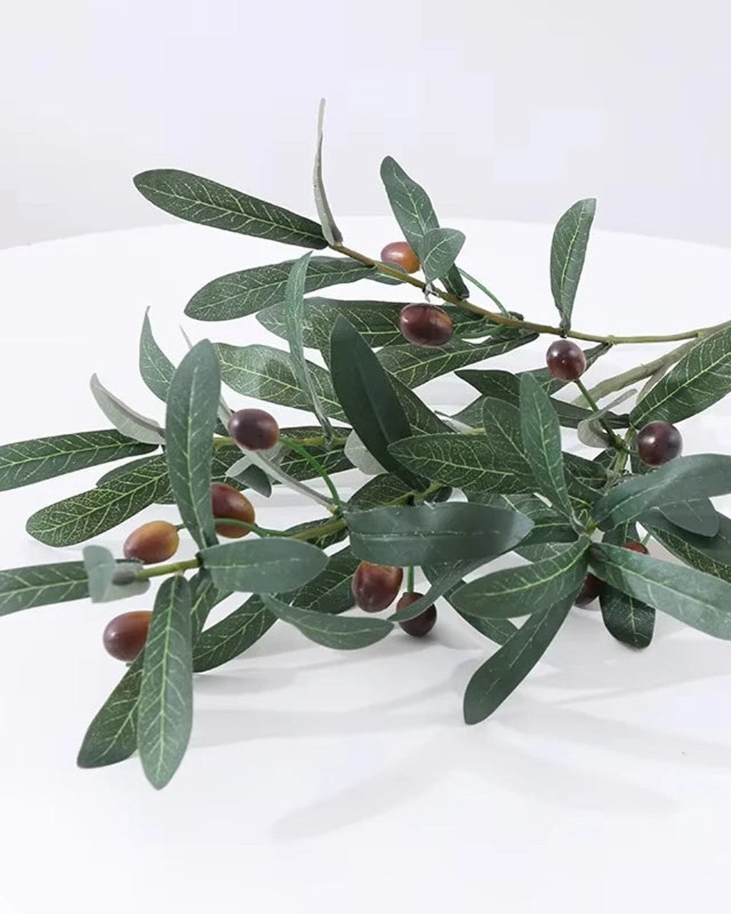 Artificial olive branch with dark olives laid on a white surface