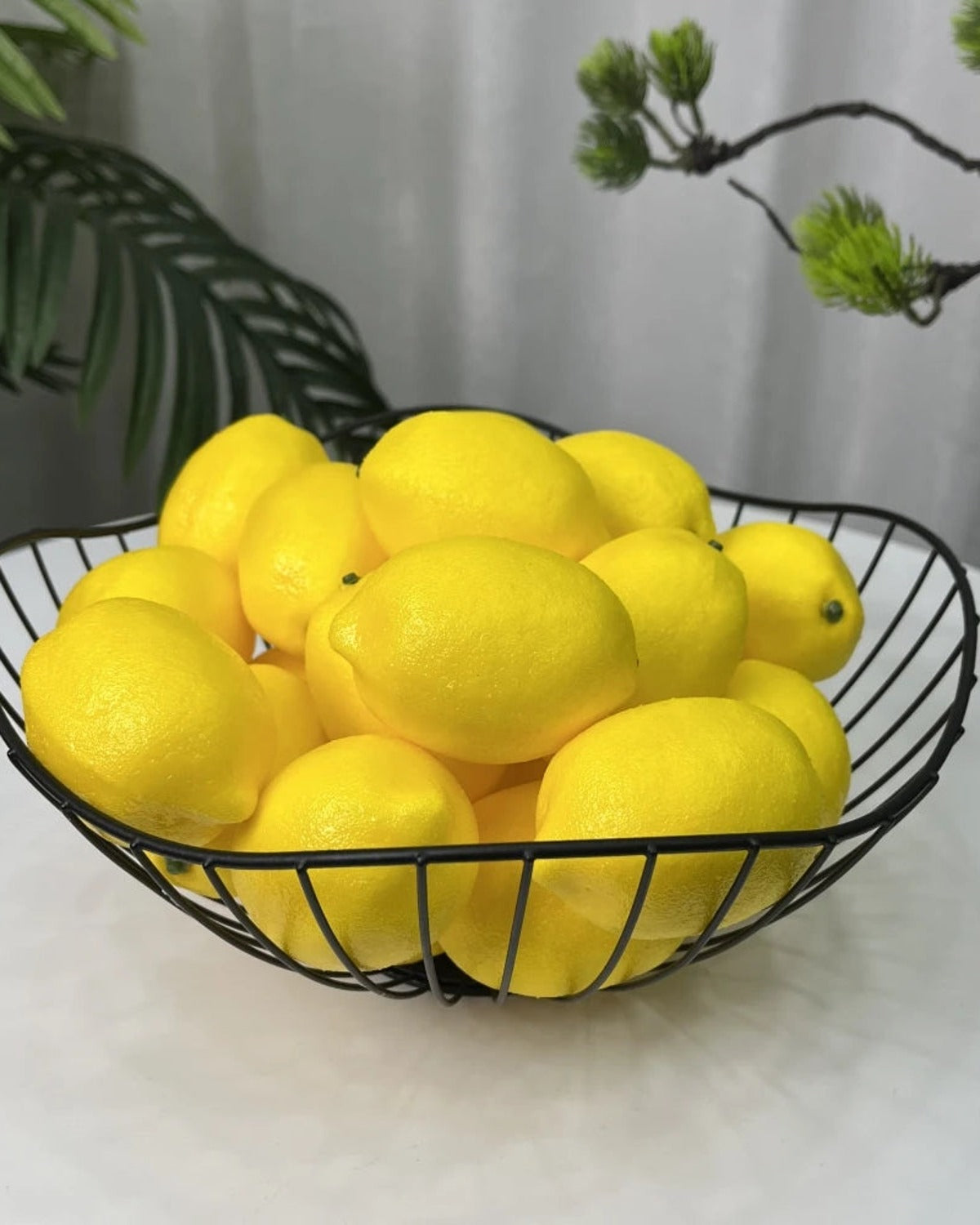 Artificial lemons piled in a black wire bowl